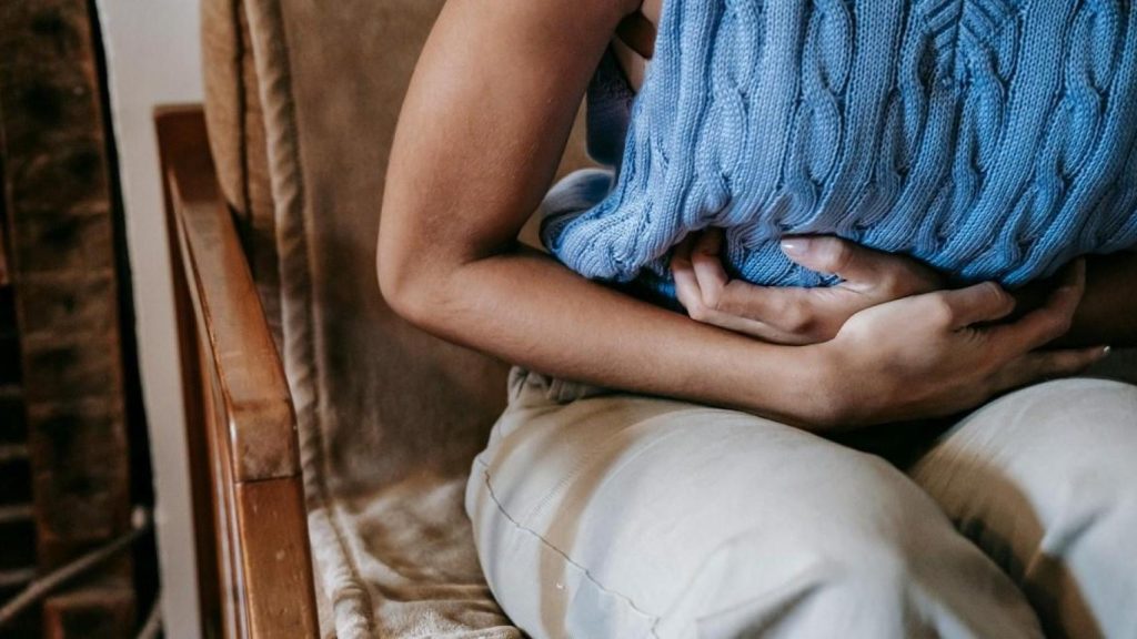 Una mujer retorciéndose de dolor mientras está sentada.